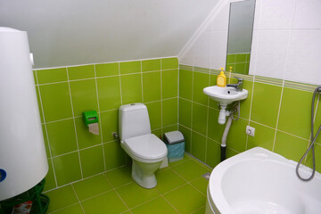 Toilet room interior with toilet bowl, electric boiler, shower, green wall tiles