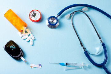 White pills in orange bottle with blood glucose meter ans stethoscope on blue background with copy...