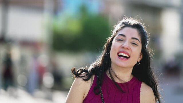 One young woman laughing and smiling at camera while standing outdoors at city in daylight