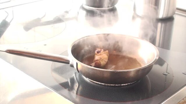 Un cuoco sistema le pentole sui fornelli mentre prepara una coscia di pollo in padella 