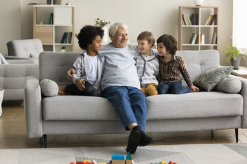Retired great-grandfather talks to three multiethnic little great-grandchildren sitting together on...