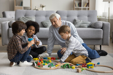 Multigenerational family play wooden railway at modern home. Senior great-grandad play railroad...