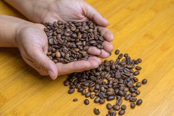 Hands holding roasted coffee beans on a table