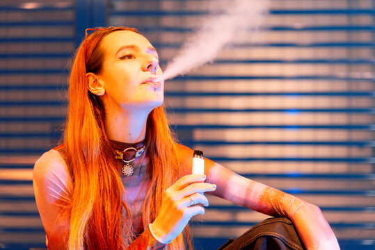 Young woman vapor exhales near blue metallic backdrop