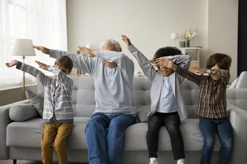 Poster Older great-grandfather and three great-grandsons sit on couch in modern living room make dab popular youth culture gesture, multigenerational family perform triumph dance have fun together at home © fizkes