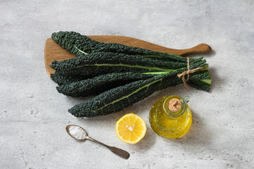Bunch of black tuscan kale (cavolo nero or lachinato kale), olive oil, lemon and salt on a gray textured background, top view - 670209541