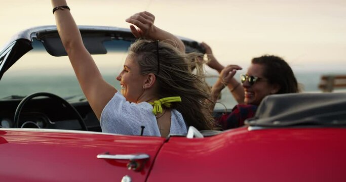 Adventure, dancing and girl friends on road trip for holiday, vacation or weekend together. Happy, freedom and young women driving a car in wind for transportation, tourism or sightseeing by coast.
