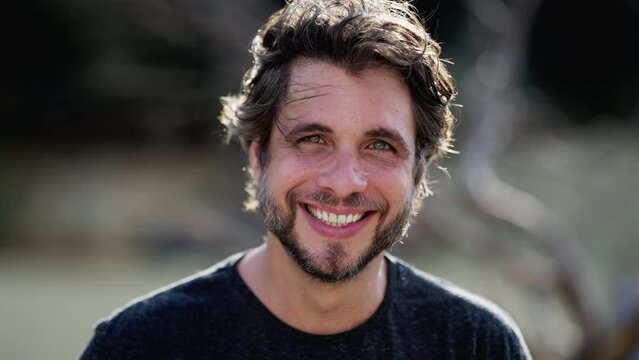 Portrait of a handsome man smiling at camera standing outdoors in sunlight. One male person in 30s with wide smile