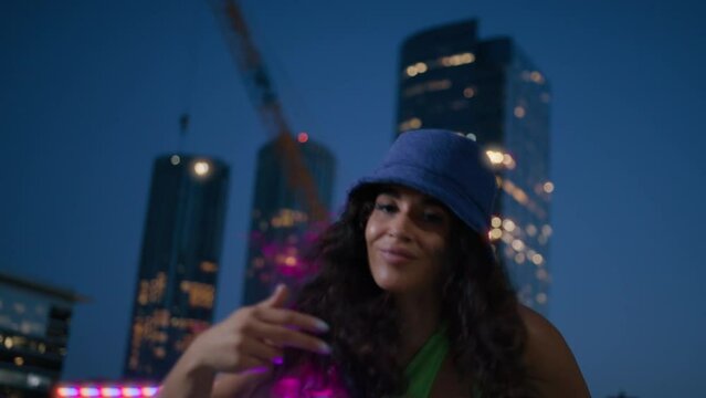 Smiling sexy girl moves hands making her long curly hair fly 4K. Portrait shot of beautiful and happy African American girl dancing at night street of cosmopolitan modern city on urban background 4K