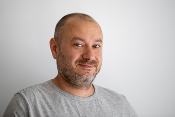 A man of ordinary appearance unshaven smiles and looks at the camera on a gray background. A man in his forties.