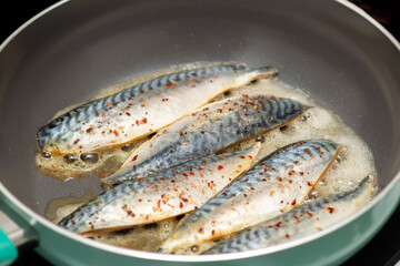 Raw fish fillet sprinkled with salt and spices is fried in a frying pan. Cooking fish.