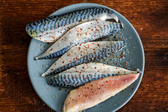 Raw fish fillet sprinkled with salt and spices on a plate on a wooden background. Mackerel fillet. View from above.