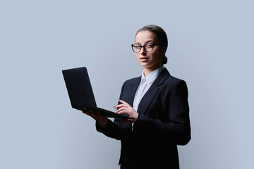 Teenage female student in formal style using computer laptop, on grey background
