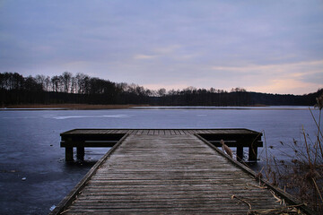 Drewniany molo na zamarzniętym jeziorze o zachodzie słońca. Zimowy wieczór.