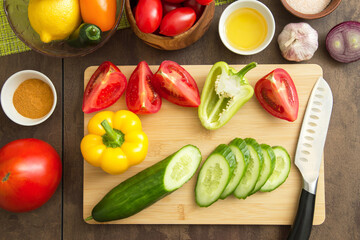 Different sliced vegetables for cooking salad on cutting board with knife on table on kitchen....