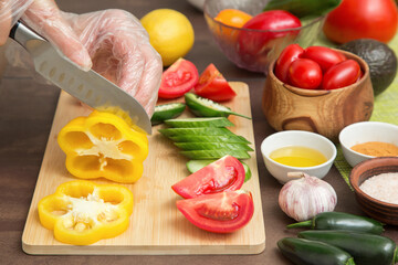 Cooking vegetables. Chef hand cutting yellow pepper and different vegetables for salad close up. Hands in gloves cooking healthy vegetarian vegan diet food