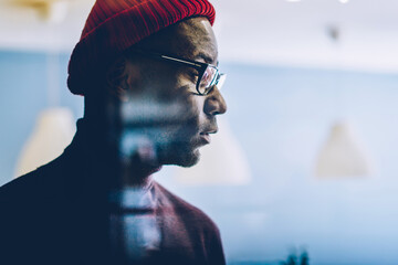 Serious african american hipster guy in spectacles looking at window pondering on ideas in office