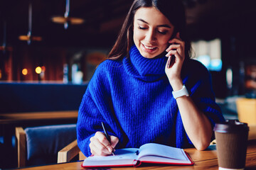 Cheerful woman with cellular phone calling to friend while studying at campus cafe
