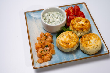 Healthy breakfast, top view. Juicy cheese pancakes with sour cream and red fish on a square plate isolated on a white background. A sprig of mint, homemade cheese curds, salty	
