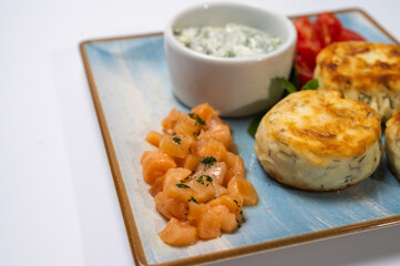 Healthy breakfast. Juicy cheese pancakes with sour cream and red fish on a square plate isolated on a white background. A sprig of mint, Homemade cheesecakes, salted 