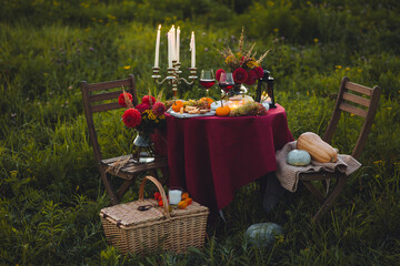 Beautiful decorated candlelight fall dinner, covered with a red tablecloth with flowers, pumpkins,...