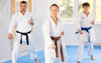 Woman and man in kimono standing in fight stance during group karate training