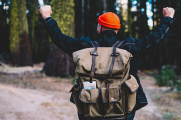 Excited male hiker with raised arms exploring natural wildness environment with green trees