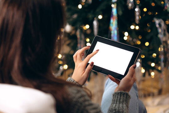 Mock-up, tablet in the hands of a girl. against the background of the New Year and Christmas tree. Concept of online shopping, discounts or online 
 communication at a distance