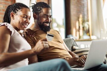 Happy African American couple using credit card during online shopping over a computer at home