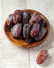 Fresh dates on a wooden plate on a white background. Oriental sweets, dried fruits