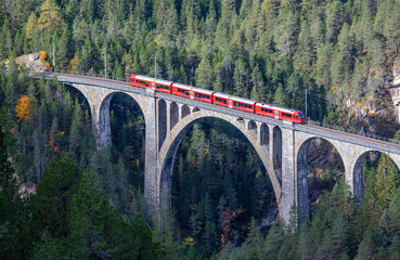 Fototapeta na wymiar A red passenger train is crossing the famous Wiesener viaduct on the train line Davos - Filisur, the highest viaduct in swiss alps