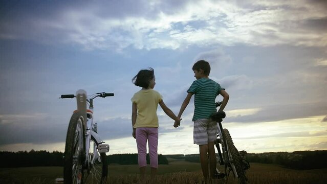 Sunset Embrace: Boy and Girl Embrace in the Field at Dusk After Bike Ride