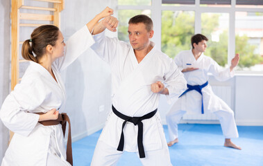 Fototapeta na wymiar Woman and man in pairs exercising karate movements during group training