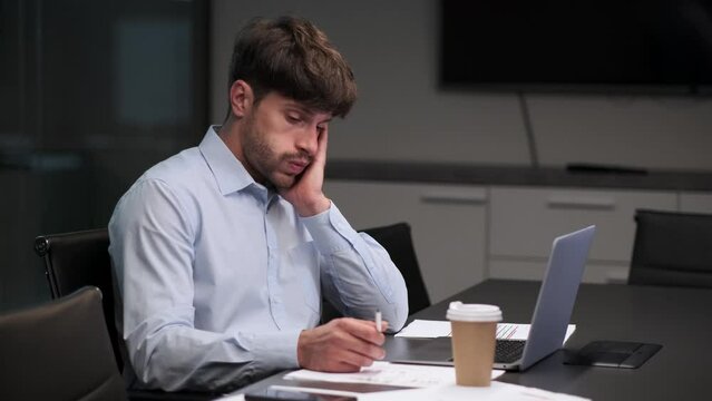 Weary man sits at desk in the office, posture reflecting the strain of overwork. Fatigue lines face as he diligently continues tasks. The quiet determination in eyes speaks of resilience.