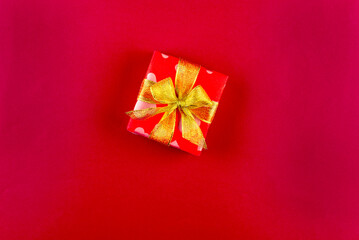 Holidays gift box wrapped in red paper with golden ribbon bow on red background. Christmas background, greeting card,