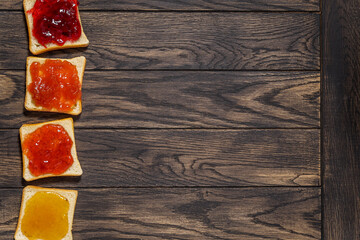 Four toasted bread with different jams on left side of table above - obrazy, fototapety, plakaty