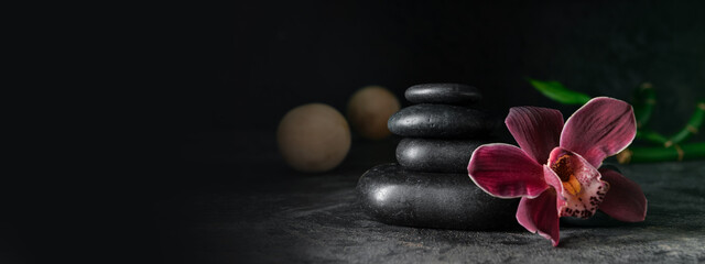 Stack of spa stones and orchid flower on dark background with space for text