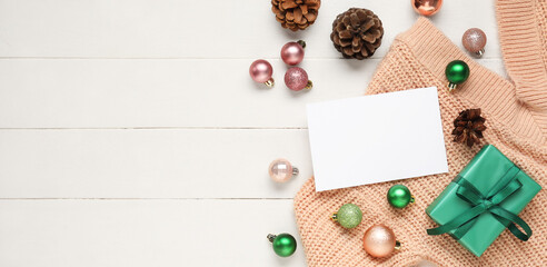 Christmas composition with blank card, gift box, sweater and decorations on white wooden background with space for text
