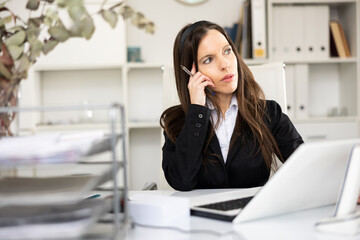 Portrait of thoughtful woman office worker sitting at table in her workplace.