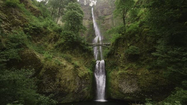 Panning shot of distant Multnomah Falls waterfall in green forest / Bridal Veil, Oregon, United States