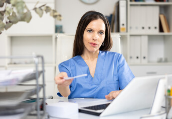 Portrait of female doctor sitting at working table and giving treatment sheet.