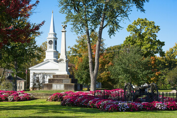 Colorful beds of flowers cluster on the town square in Twinsburg, Ohio, with in front of the civil war monument and a historic old church. - obrazy, fototapety, plakaty
