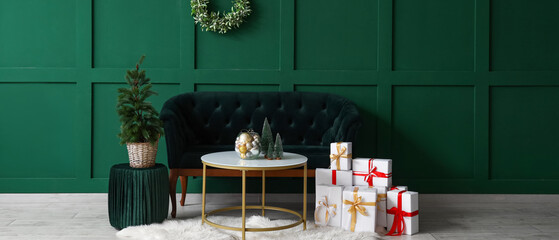 Interior of festive living room with dark green sofa, coffee table, gifts and Christmas decorations