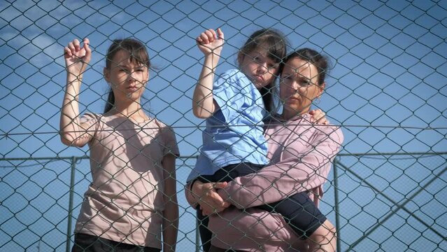 Refugee problems. Sad woman with children behind a wire fence.