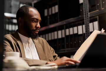 African american prosecutor preparing for case, studying crime matter files in police office. Cop reading forensic expertise report and analyzing investigation clues at night time