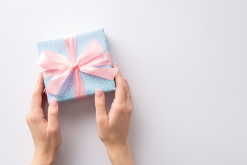 Guess what's in my hands? First person top view girl's hands holding delightful pastel blue gift box with polka dots and a dainty pink ribbon bow. Celebrate with me in style on this white canvas