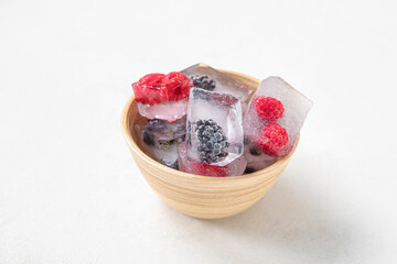 Bowl with frozen berries in ice cubes on white background