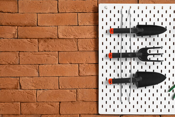 Pegboard with gardening tools on brick wall, closeup