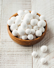 Cranberries in powdered sugar on a wooden plate on a white wooden background. 
