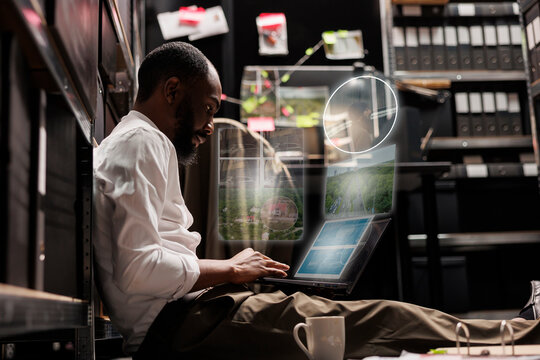 Professional detective working with holograms, planning private investigation with holographic evidence and insight in archive room. Young investigator examining artificial intelligence.
